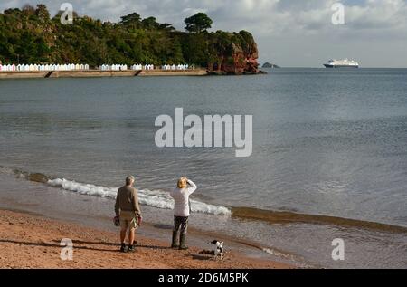 Hundewanderer am Strand von Goodrington und betrachten das Kreuzfahrtschiff Zaandam, das während der Coronavirus-Pandemie in Tor Bay vor Anker lag. Stockfoto