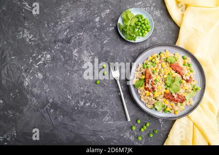 Quinoa-Haferbrei mit grüner Erbse, Mais und getrockneten Tomaten auf Keramikplatte auf grauem Betongrund und gelbem Textil. Draufsicht, flach liegend, Kopie sp Stockfoto