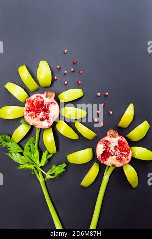 Die Blumen bestehen aus Granatapfel, Äpfeln und Sellerie auf schwarzem Hintergrund. Gesunde Ernährung und Vegetarismus Konzept Stockfoto