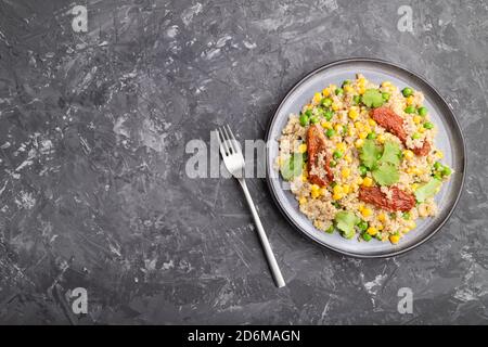 Quinoa-Haferbrei mit grüner Erbse, Mais und getrockneten Tomaten auf Keramikplatte auf grauem Betongrund. Draufsicht, flach liegend, Kopierbereich. Stockfoto