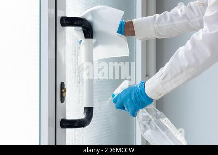 Hände mit Nitrilhandschuhen und einer hydroalkoholischen Lösung sprühen Der Türgriff, um Coronavirus mit Einwegpapier zu verhindern Stockfoto