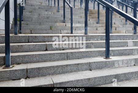 Externe mehrstufige Steintreppe. Es gibt viele Treppen und Geländer aus Metall. Viele Schritte in einer städtischen Umgebung, symbolisch abstrakt zurück Stockfoto