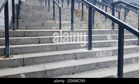 Externe mehrstufige Steintreppe. Es gibt viele Treppen und Geländer aus Metall. Viele Schritte in einer städtischen Umgebung, symbolisch abstrakt zurück Stockfoto