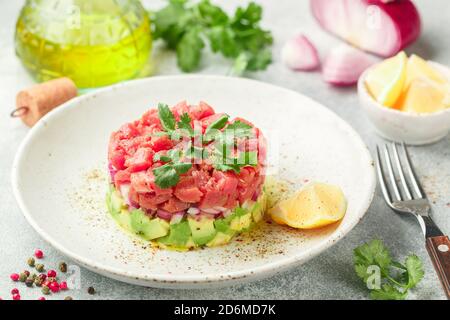 Thunfisch-Tartar mit Avocado und lila Zwiebel. Serviert mit Koriander, Zitrone und frisch gemahlenem Pfeffer. Köstliche Vorspeise (Salat) von r Stockfoto