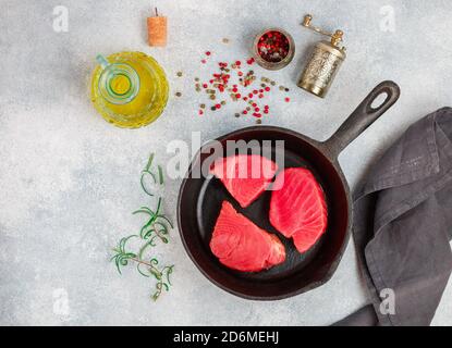 Rohe Thunfischsteaks mit Meersalz, rosa, grünem und schwarzem Pfeffer und Rosmarin zum Grillen oder Kochen in einer gusseisernen Pfanne. Bereiten Sie ein köstliches Abendessen. Sel Stockfoto