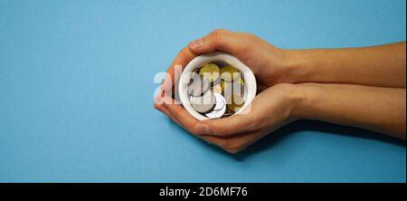 Zwei Hände halten eine Schüssel mit Münzen auf einem blauen Hintergrund. Eine Tasse Geld. In ein Unternehmen investieren. Finanzielle Unterstützung für die Armen. Webbanner für die Website. Stockfoto