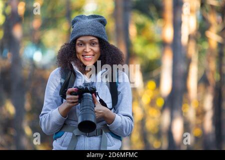 Lächelnde afroamerikanische Frau im Wald mit einer Kamera. Sie beobachtet und fotografiert Vögel. Stockfoto