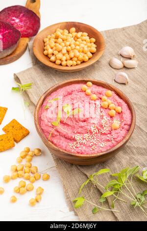 Hummus mit Rüben und mikrogrünen Basilikum Sprossen in Holzschüssel auf weißem Holzhintergrund und Leinentextilien. Seitenansicht, Nahaufnahme. Stockfoto