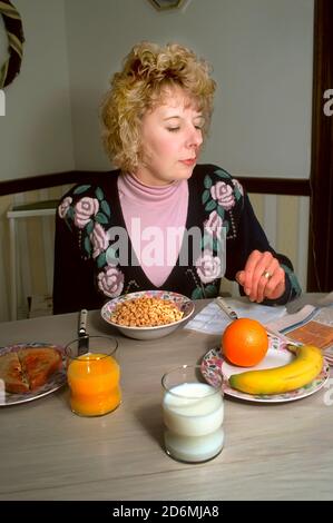 Erwachsene Frauen essen ein gesundes Frühstück mit Müsli, Saft, Milch und Obst, während sie die Zeitung lesen Stockfoto