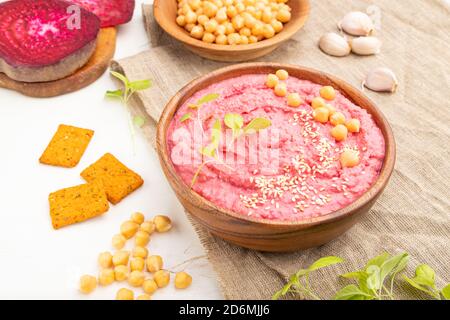 Hummus mit Rüben und mikrogrünen Basilikum Sprossen in Holzschüssel auf weißem Holzhintergrund und Leinentextilien. Seitenansicht, Nahaufnahme. Stockfoto