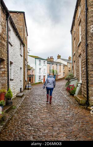 Person, die durch die gepflasterten Straßen des Dorfes Cumbrian aufwacht Von Dent in Dentdale im Yorkshire Dales Nationalpark Cumbria England Großbritannien Stockfoto