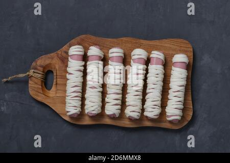 Wurst Mumien in Teig vor dem Backen. Essen für Halloween auf Holzbrett. Kochidee für Kinder. Stockfoto