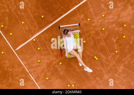 Portrait einer lächelnden Frau, die sich nach hartem Tennistraining im Freien auf dem Tennisplatz mit vielen Bällen und Schlägern entspannt. Dolly-Schuss. Draufsicht Stockfoto