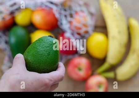 Die Frau hält Avocado in der Hand. Frische Früchte sind im Hintergrund. Stockfoto