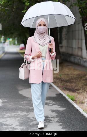 Junge muslimische Frau in Hijab, Schutzmaske und Casualwear Chillen im Park Stockfoto