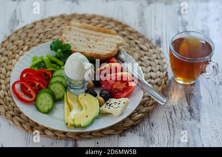 Gesundes Keto-Diät-Frühstück: Gekochtes Ei, Avocado, Käse, Gurke, Pfeffer, Tomaten, Petersilie, Vollkornbrot und Tee Stockfoto