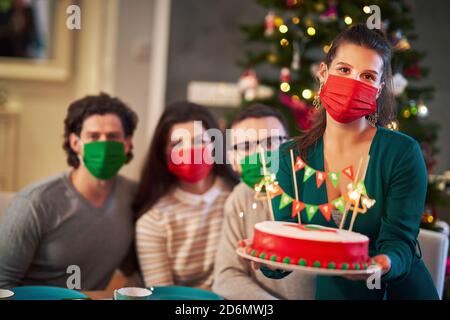 Gruppe von Freunden in Masken feiern Weihnachten zu Hause mit Schicker Kuchen Stockfoto