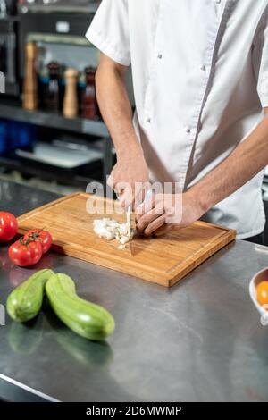 Hände des jungen männlichen Küchenchefs schneiden frische Zwiebeln auf Holz Tafel nach Tisch Stockfoto