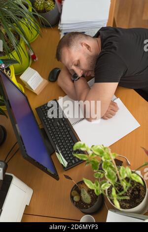Männlicher Manager schläft am Arbeitsplatz. Ermüdung, Überlastung und Terminkonzept. Blick von oben. Stockfoto