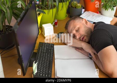 Männlicher Manager schläft am Arbeitsplatz. Ermüdung, Überlastung und Terminkonzept. Stockfoto