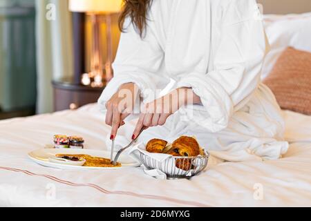 Frau beim Frühstück im Bett. Frisches Croissant Brot Obst auf dem Teller Stockfoto