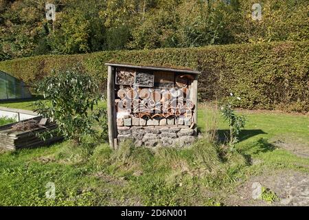 Insektenhotel mit Steinen, alten Fliesen, gebohrten Löchern in Baumstämmen, Rinde, Bambus, Lehm und mit Unterschlupf für Schmetterlinge.Holländischer Garten im Herbst. Stockfoto