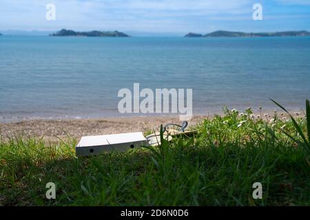 Ein paar Jandals und eine leere Pizzabox am Strand Im malerischen man O war Bay auf Waiheke Island New Seeland Stockfoto