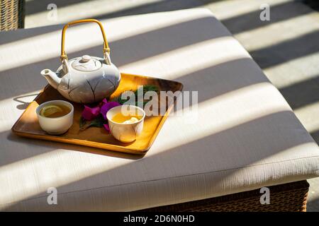 Asiatische weiße Teekanne glasierte Tonschüsseln Tassen für grünen Tee Auf Holztablett im Spa mit Sonnenschirmen Stockfoto