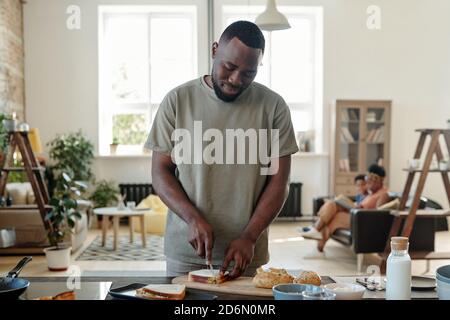 Junger bärtiger Mann afrikanischer Herkunft bereitet Sandwiches zum Frühstück zu Stockfoto