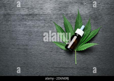 Eine Flasche mit CBD-Cannabis oder Hanföl auf dem Marihuanablatt auf dem schwarzen Holzhintergrund mit Kopierraum. Konzept der alternativen Medizin Stockfoto