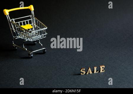 Warenkorb und die Aufschrift 'Sale' auf schwarzem Hintergrund. Schwarzer Freitag, Rabatte, Verkauf, Einkaufen, Zinsschild. Leerzeichen für Text Stockfoto