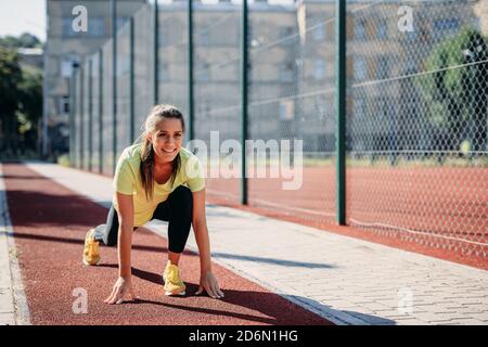Fröhliche Frau, die vor dem Laufen in Startposition steht Stockfoto