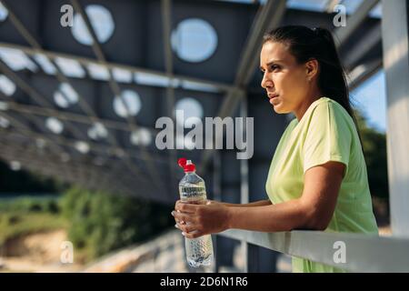 Müde Frau hält Flasche Wasser nach dem Training Stockfoto
