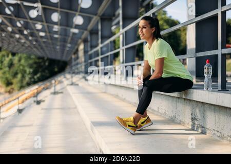 Sportliche Frau sitzt im Stadion mit einer Flasche Wasser Stockfoto