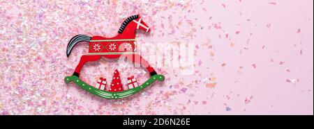 Weihnachts-Spielzeug von Schaukelpferd auf rosa Hintergrund mit Glitzer. Flach legen Stockfoto