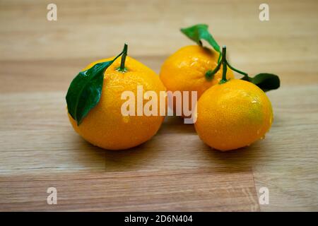 Drei reife Mandarinen mit grünen Blättern und Wassertropfen. Orange Mandarine Orange Frucht auf einem Holztisch Nahaufnahme Stockfoto