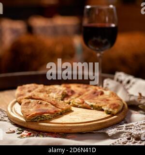 Glas Rotwein und Stücke von placida mit Quark oder Vertuta auf einem Holztablett, Nahaufnahme, traditionelle rumänische, moldawische oder Balkan-Kuchen Stockfoto