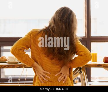 Rückansicht der gesichtslosen jungen Frau, die den Rücken berührt Gefühl von Rückenschmerzen, Unwohlsein Stockfoto