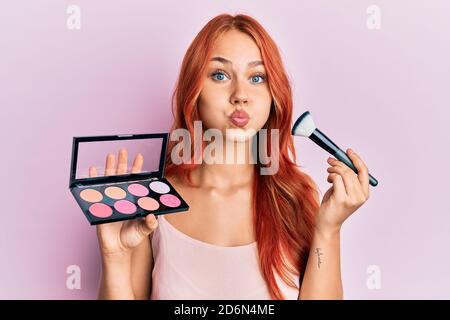 Junge Rotschopf Frau hält Make-up und Pinsel Puffing Wangen mit lustigen Gesicht. Mund mit Luft aufgeblasen, fangen Luft. Stockfoto