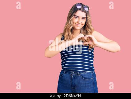 Junge kaukasische Frau trägt lässige Kleidung und Sonnenbrille lächelt in der Liebe zeigt Herz Symbol und Form mit Händen. Romantisches Konzept. Stockfoto