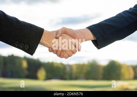 Handshake zweier moderner erfolgreicher Geschäftspartner gegen grüne Bäume Stockfoto