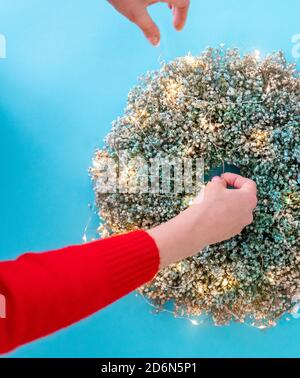 Weibliche Hände dekorieren weihnachtskranz mit Girlande, Draufsicht Stockfoto