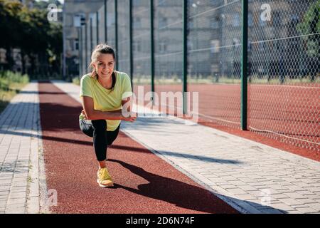 Lächelnde Sportlerin dehnt den Körper vor dem Lauftraining aus Stockfoto