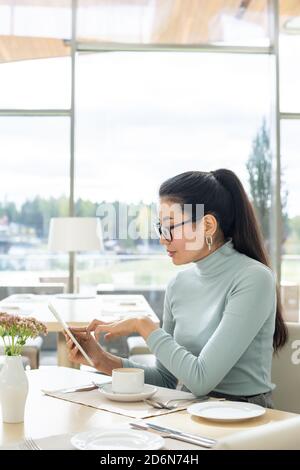 Junge zeitgenössische Geschäftsfrau der asiatischen Ethnie zeigt auf Tablet-Display Stockfoto