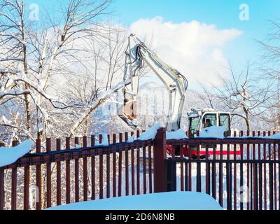 Ein Bagger hinter einem Zaun arbeitet in einem Bergtal An einem klaren Wintertag Stockfoto