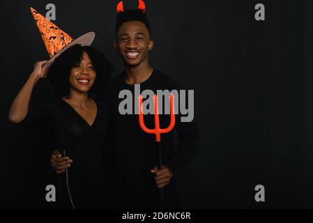 Zwei afroamerikanische Freunde feiern Halloween im Studio in Kostümen auf schwarzem Hintergrund. Stockfoto