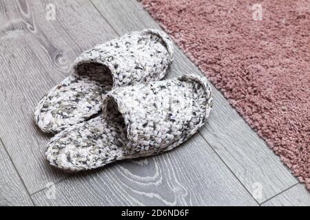 Weiße Strickschuhe stehen auf einem grauen Holzboden in der Nähe Pinker Teppich Stockfoto