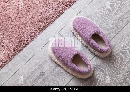 Kuschelige Wollschuhe stehen auf grauem Holzboden in der Nähe von rosa Teppich Stockfoto