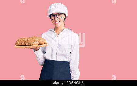 Schöne Brünette junge Frau trägt Bäcker Uniform hält hausgemachtes Brot Schauen positiv und glücklich stehen und lächeln mit einem selbstbewussten Lächeln Sie Stockfoto