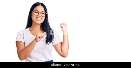 Junge schöne asiatische Mädchen tragen lässige Kleidung und Brille zeigt auf den Rücken hinter mit Hand und Daumen nach oben, lächelnd zuversichtlich Stockfoto